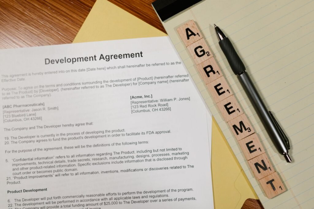 Close-up of a development agreement document with pen and Scrabble tiles spelling 'AGREEMENT.'
